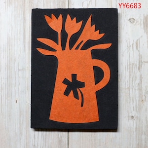 Puede incluir: Corte de fieltro naranja de un jarrón con un diseño floral en la parte delantera, lleno de tulipes. El jarrón y las tulipes están cortados de fieltro naranja y colocados sobre un fondo de fieltro negro.