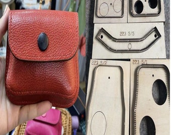 May include: A red leather wallet with a flap closure and a metal button. The wallet is being held in a hand. There are five wooden cutting dies with different shapes and sizes, including a rectangle with two circles, a curved shape, a rectangle with one circle, and a rectangle with two circles. The dies are labeled with numbers and fractions.