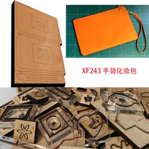 Puede incluir: Un conjunto de herramientas de artesanía de cuero para hacer una cartera de mano. Las herramientas incluyen un patrón para la cartera, una matriz para cortar el cuero y una variedad de otras herramientas. Las herramientas están hechas de madera y metal. La imagen también muestra una cartera de mano de cuero naranja terminada.