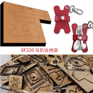May include: A set of leather craft dies for making a headphone holder. The dies are made of clear plastic and are arranged in a pile. The dies include shapes such as a heart, a flower, and a rectangle. The dies are used to cut leather to create the headphone holder. The image also shows a red leather headphone holder with a key chain.