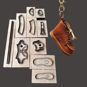May include: A brown leather boot keychain hangs next to a collection of metal die-cut shapes on wooden blocks. The die-cut shapes are various sizes and shapes, likely for leather crafting. The boot keychain has a gold-colored clasp.