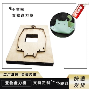 May include: A wooden die-cutting template shaped like a cat with a square opening in the center. The template is used to cut out leather or fabric for crafting projects. The image also shows a finished cat-shaped leather pouch.