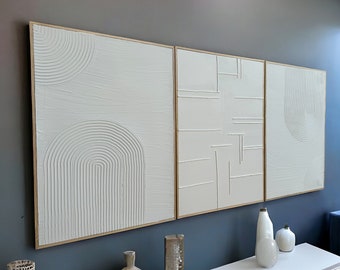 May include: Three white framed canvas wall art pieces with raised geometric designs. The canvases are arranged horizontally on a dark blue wall. The leftmost canvas features a series of concentric circles, the middle canvas features a series of intersecting lines, and the rightmost canvas features a series of concentric circles.