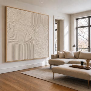Op de afbeelding: Een groot rechthoekig wandkunstwerk met een beige getextureerd oppervlak met verhoogde, concentrische halfronde boogpatronen. Het kunstwerk is ingelijst in lichtgekleurd hout en toont een mix van ruwe secties en gladde, lineaire groeven.
