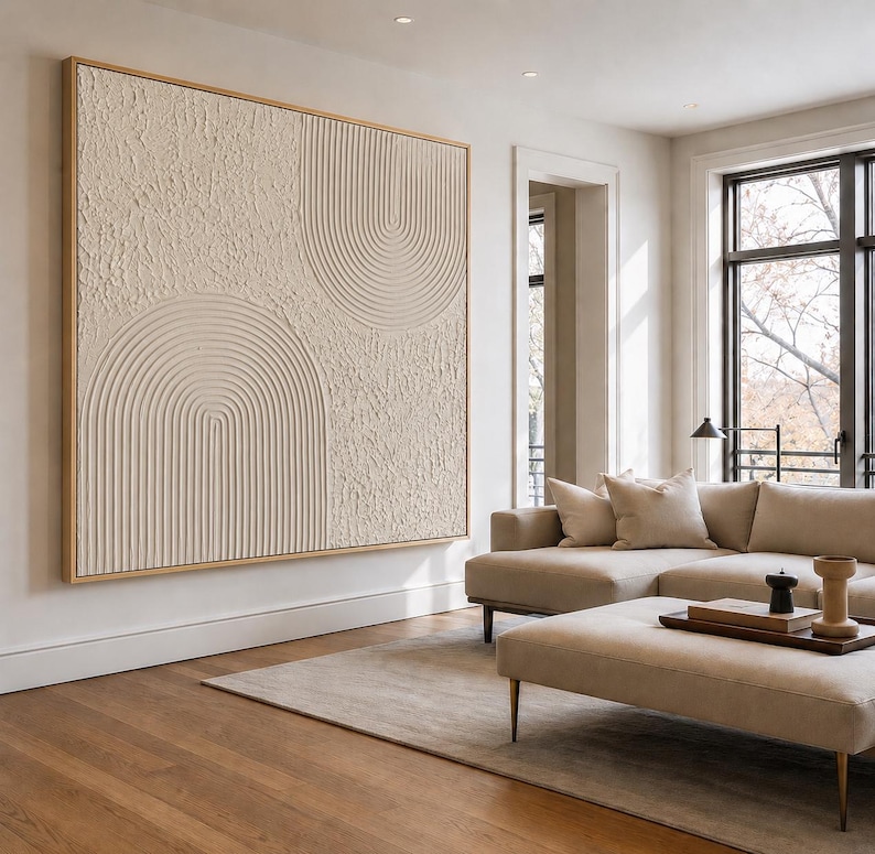 Op de afbeelding: Een groot rechthoekig wandkunstwerk met een beige getextureerd oppervlak met verhoogde, concentrische halfronde boogpatronen. Het kunstwerk is ingelijst in lichtgekleurd hout en toont een mix van ruwe secties en gladde, lineaire groeven.