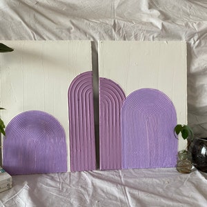 May include: Two white canvases with a textured, raised, lavender-colored design of arches. The arches are layered on top of each other and have a striped pattern.