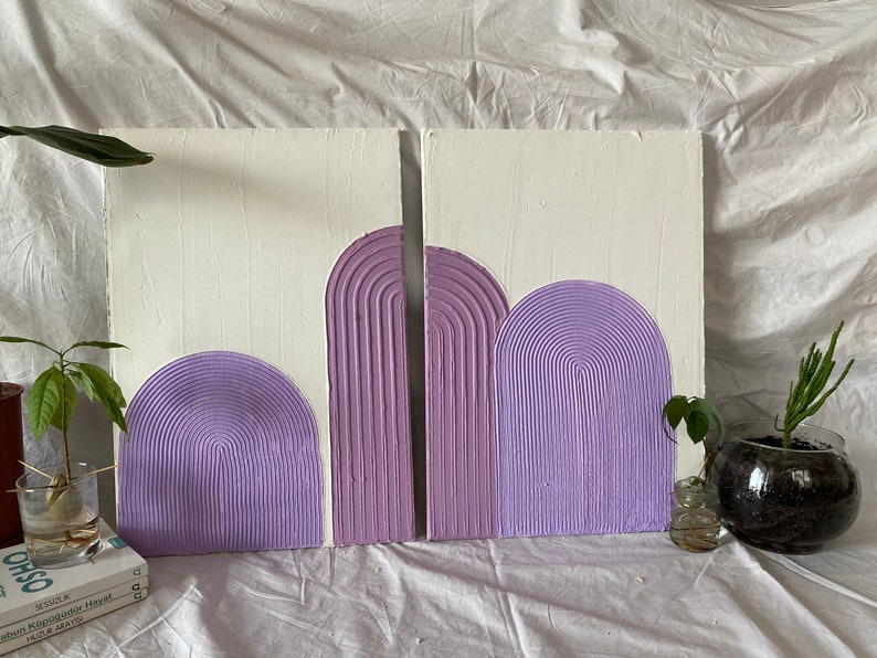 May include: Two white canvases with a textured, raised, lavender-colored design of arches. The arches are layered on top of each other and have a striped pattern.