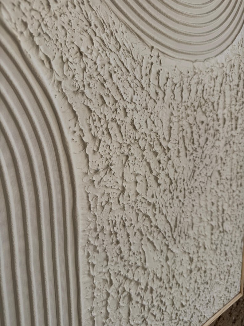 Op de afbeelding: Een gestructureerd wandkunstwerk in een neutraal gebroken wit kleurenpalet. Het oppervlak toont een combinatie van verhoogde, parallelle gebogen lijnen en een dicht, ruw impasto-gedeelte met diepe richels en pieken door dikke verf.