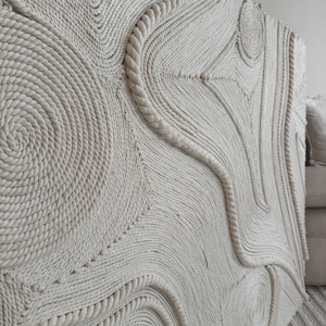 K&ouml;nnte beinhalten: Ein gro&szlig;er Wandbehang aus geflochtenem Seil mit einem einzigartigen abstrakten Design mit wirbelnden Mustern und Kurven. Das Seil ist hellbeige und erzeugt einen neutralen und strukturierten Look.