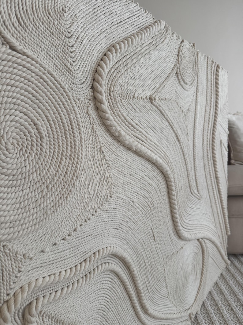 K&ouml;nnte beinhalten: Ein gro&szlig;er Wandbehang aus geflochtenem Seil mit einem einzigartigen abstrakten Design mit wirbelnden Mustern und Kurven. Das Seil ist hellbeige und erzeugt einen neutralen und strukturierten Look.