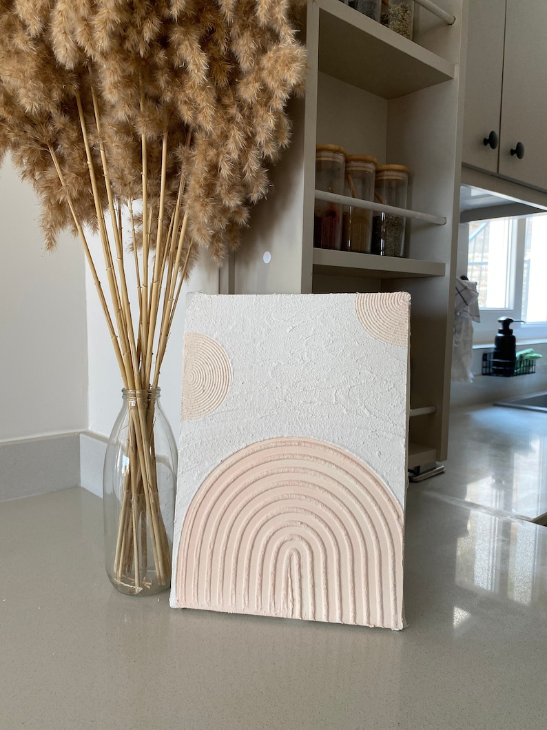 May include: A white textured canvas with a pink raised rainbow design and two white circles.