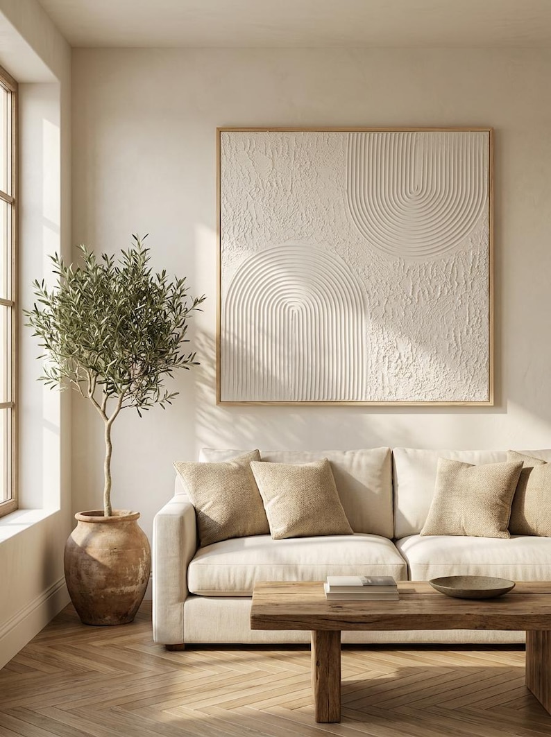Op de afbeelding: Een vierkant kunstwerk aan de muur met een wit gestructureerd oppervlak met verhoogde boogpatronen, ingelijst in licht hout. Het kunstwerk toont een combinatie van gladde, concentrische halfronde lijnen en ruwe, onregelmatige secties.