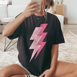 May include: A black t-shirt with a pink lightning bolt graphic. The shirt is oversized and has a relaxed fit.