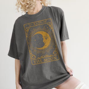 May include: A dark gray oversized t-shirt with a vintage tarot card design featuring a crescent moon and the text "XVIII THE MOON".