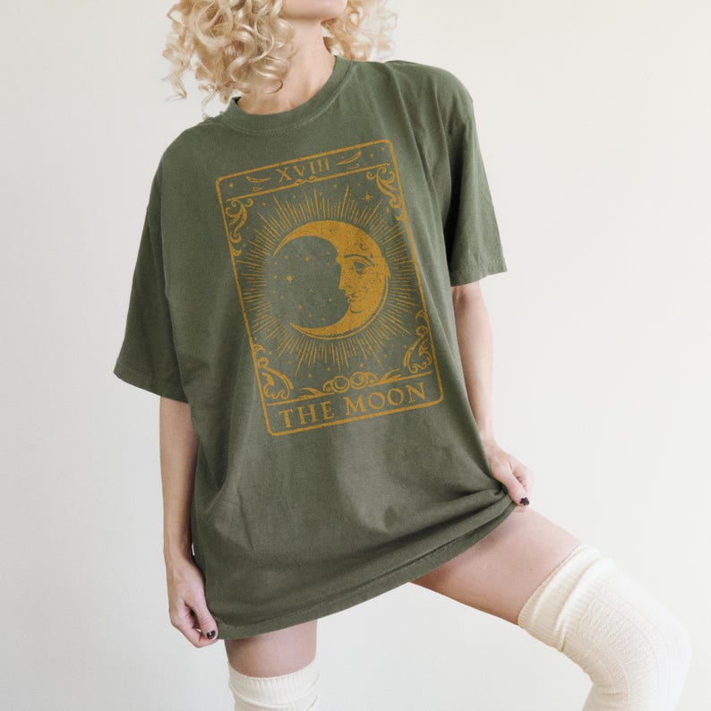 May include: A green oversized t-shirt with a vintage tarot card design featuring a crescent moon with a face and the text "XVIII THE MOON".
