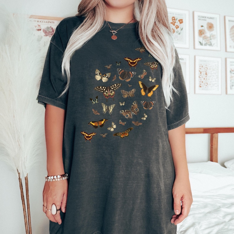 K&ouml;nnte beinhalten: Ein dunkelgraues Oversize-T-Shirt mit einem Vintage-Druck verschiedener Schmetterlinge in Braun-, Gelb- und Oranget&ouml;nen.