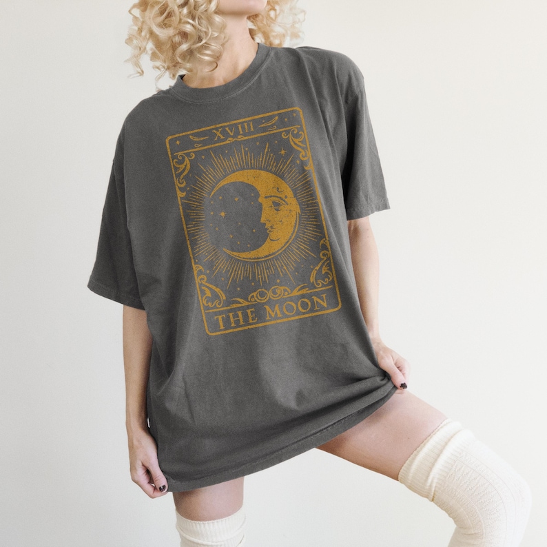 May include: A dark gray oversized t-shirt with a vintage tarot card design featuring a crescent moon and the text "XVIII THE MOON".
