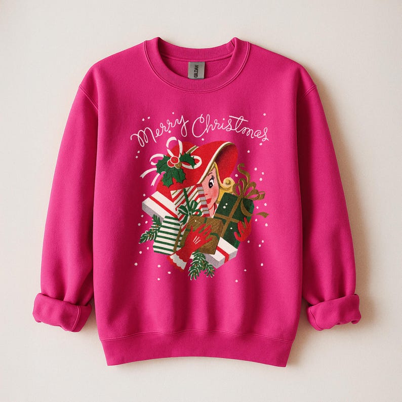 May include: A fuchsia sweatshirt with a festive Christmas design. The graphic features a woman in a red hat holding gifts, with the words "Merry Christmas" in cursive. White polka dots and green accents complete the holiday theme.