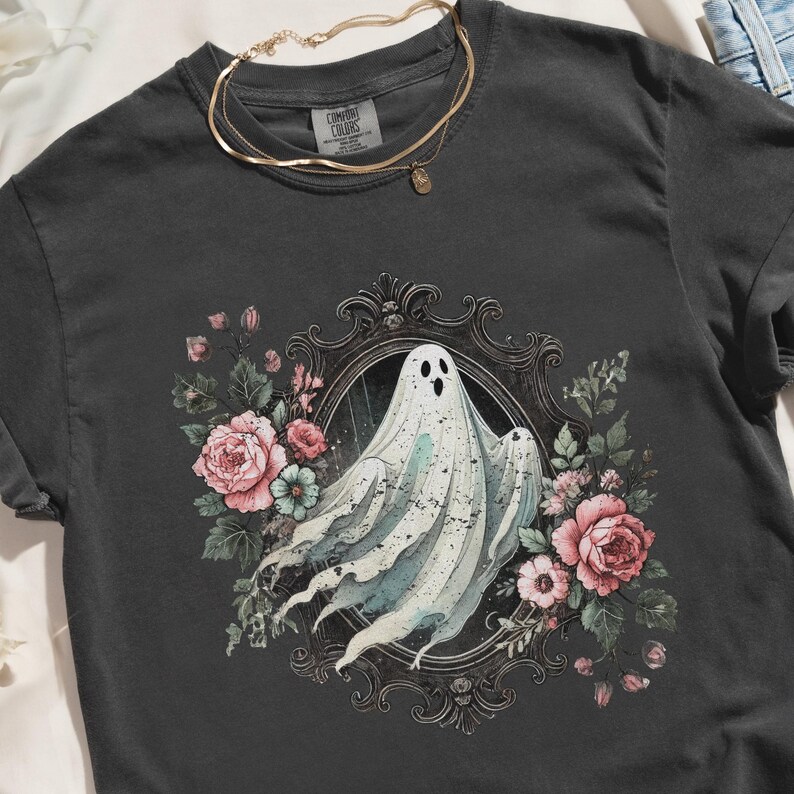 Puede incluir: Una camiseta negra con un gr&aacute;fico vintage de un fantasma en un marco floral. El fantasma es blanco y transl&uacute;cido, y el marco est&aacute; decorado con rosas rosas y hojas verdes.