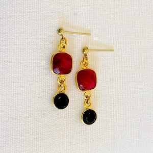 May include: A pair of dangle earrings featuring red and black gemstones. The earrings have a gold chain and a gold post.
