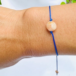 Può includere: Un braccialetto di corda blu con un unico perno rotondo di colore arancione e bianco.