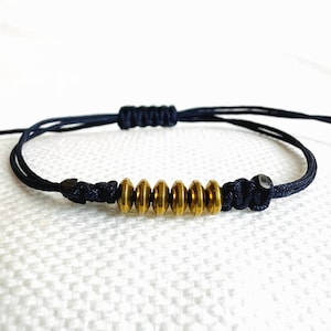 Peut inclure: Un bracelet en cordon noir avec une rangée de perles en métal doré.