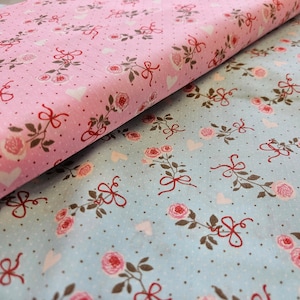 Op de afbeelding: Twee stukken stof met een bloemenpatroon. De bovenste stof is roze met witte stippen en een rood strikpatroon. De onderste stof is lichtblauw met witte stippen en een rood strikpatroon.