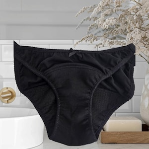 Könnte beinhalten: Schwarze Unterwäsche aus Baumwolle mit einer schwarzen Schleife auf der Vorderseite. Die Unterwäsche hat einen eingebauten Einsatz für zusätzlichen Schutz.