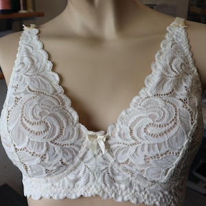 May include: Ivory-colored lace bra with a delicate floral pattern. The bra features scalloped edges, adjustable straps, and small bow accents. The intricate design and soft color create a feminine and elegant look. This lingerie piece is designed for comfort and style.