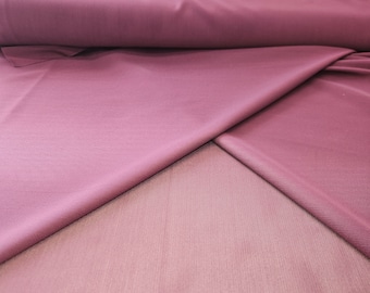 May include: A close-up of two layers of mauve fabric. The top layer is smooth and the bottom layer is a sheer mesh.