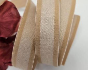 May include: Beige elastic trim with a satin stripe down the center. The trim is rolled up and ready to be used for sewing projects.