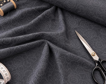 May include: A dark gray fabric featuring a tonal floral pattern with intricate circular motifs. The textile is displayed with a spool of gray thread, a pair of metal scissors with black handles, and a white measuring tape showing centimeters.