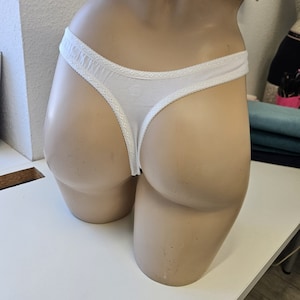 Könnte beinhalten: Weiße Baumwoll-String-Unterwäsche mit Spitzenbesatz. Die Unterwäsche befindet sich auf einer Schaufensterpuppe.