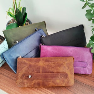 May include: Five leather pouches in different colors and textures. The pouches are arranged on a wooden surface. The pouches are all closed and have a zipper closure.