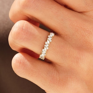 Op de afbeelding: Een gouden ring met een band bezet met marquise-geslepen edelstenen. De ring heeft meerdere kleine, heldere edelstenen gerangschikt in een doorlopend patroon. De ring wordt om een vinger gedragen.