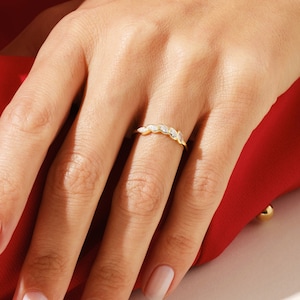 Puede incluir: Un delicado anillo de banda de oro con una fila de pequeñas piedras ovaladas transparentes.