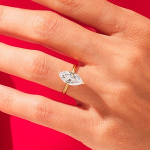 May include: A gold ring with a large, clear marquise-shaped diamond set in a simple band.