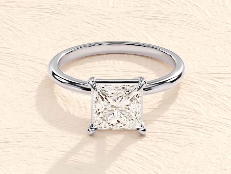 May include: A silver ring with a square-shaped diamond set in a prong setting.