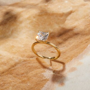 May include: A gold ring with a square-shaped diamond set in the center.