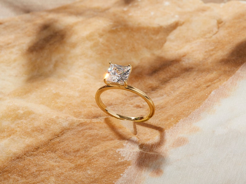 May include: A gold ring with a square-shaped diamond set in the center.