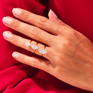 May include: A hand wearing three gold rings with marquise-shaped clear stones. The rings are stacked on each other, with the largest ring on the bottom and the smallest ring on top.