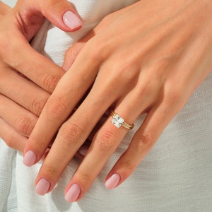 May include: A close-up of a hand wearing a gold ring with a large, square-shaped diamond. The ring is set with smaller diamonds on the band.
