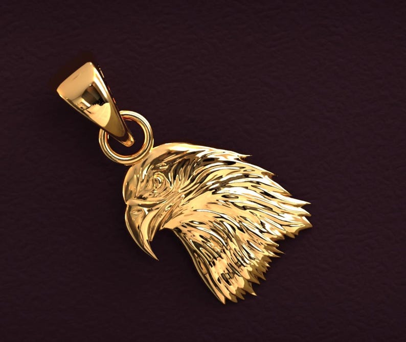 May include: A gold-colored pendant shaped like an eagle's head. The pendant features detailed feather textures and a loop for a chain. The eagle's beak is slightly open, and the overall design is highly polished.
