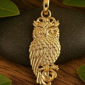 May include: A gold-colored owl pendant with intricate detailing. The pendant features an owl with detailed feathers, large eyes, and a decorative perch. The pendant is suspended from a matching gold bail. The owl is approximately 2 inches in height.