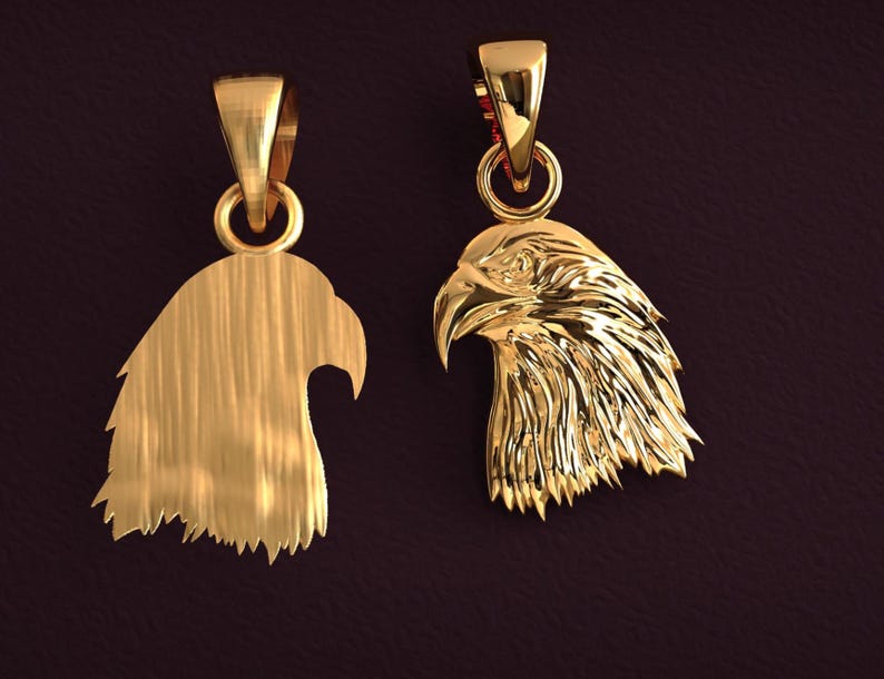May include: Two gold-colored eagle head pendants. One pendant is a solid silhouette, while the other features detailed feathering. Both have a loop for a chain. The pendants are displayed against a dark background.