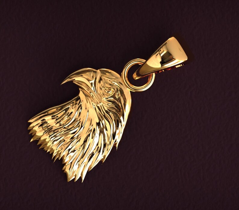 May include: A gold-colored pendant in the shape of an eagle's head. The pendant features detailed feather and beak carvings, with a loop for a chain. The background is a dark, textured brown.