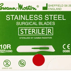 Puede incluir: Un paquete verde y blanco de 10R cuchillas quirúrgicas estériles. El paquete está etiquetado con "Swann-Morton" y "Cuchillas quirúrgicas de acero inoxidable". Las cuchillas están esterilizadas por radiación gamma. El paquete también incluye una marca CE y un número de referencia.