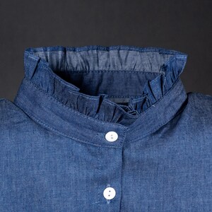 K&ouml;nnte beinhalten: Ein blaues Jeanshemd mit R&uuml;schenkragen und wei&szlig;en Kn&ouml;pfen.