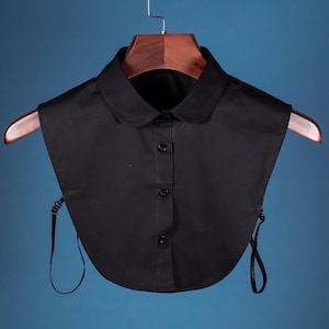 May include: A black faux collar with a button closure and adjustable straps. The collar is made of a smooth, cotton-like fabric.