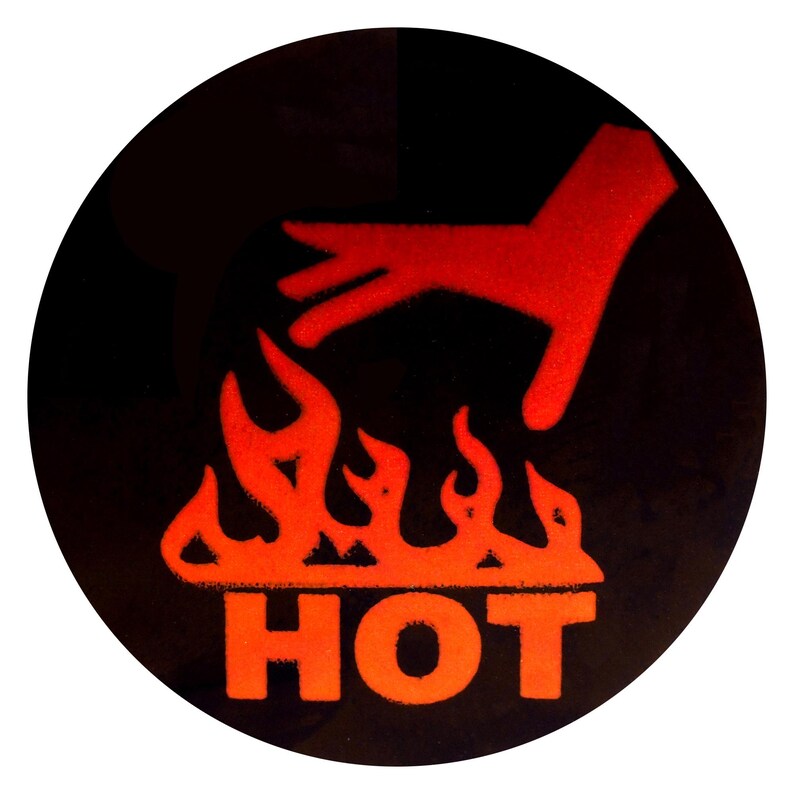 Op de afbeelding: Een ronde, zwarte sticker met een rode afbeelding. De afbeelding toont een hand boven vlammen, met het woord "HOT" in oranje eronder. Het ontwerp is een waarschuwingssymbool.